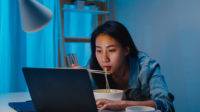 ilustrasi perempuan membuka laptop dan makan mie instan saat begadang (freepik)